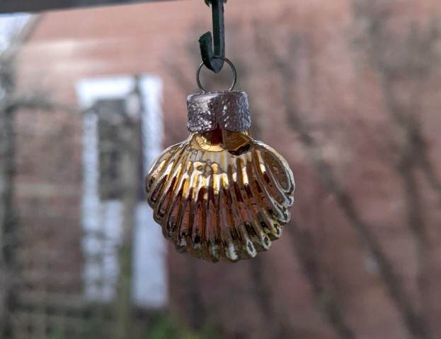Small gold glass bauble shaped like a scallop shell, hanging in a window