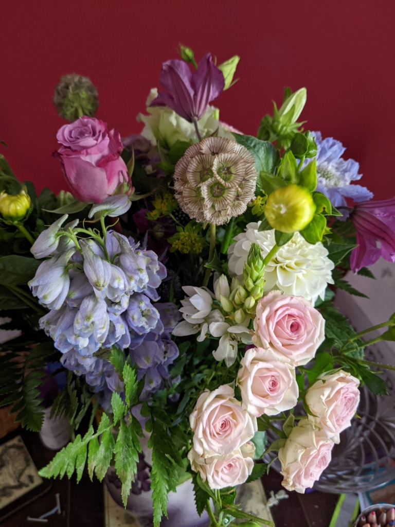 Bouquet of flowers in shades of pink, blue, mauve, and pale green, against a red wall