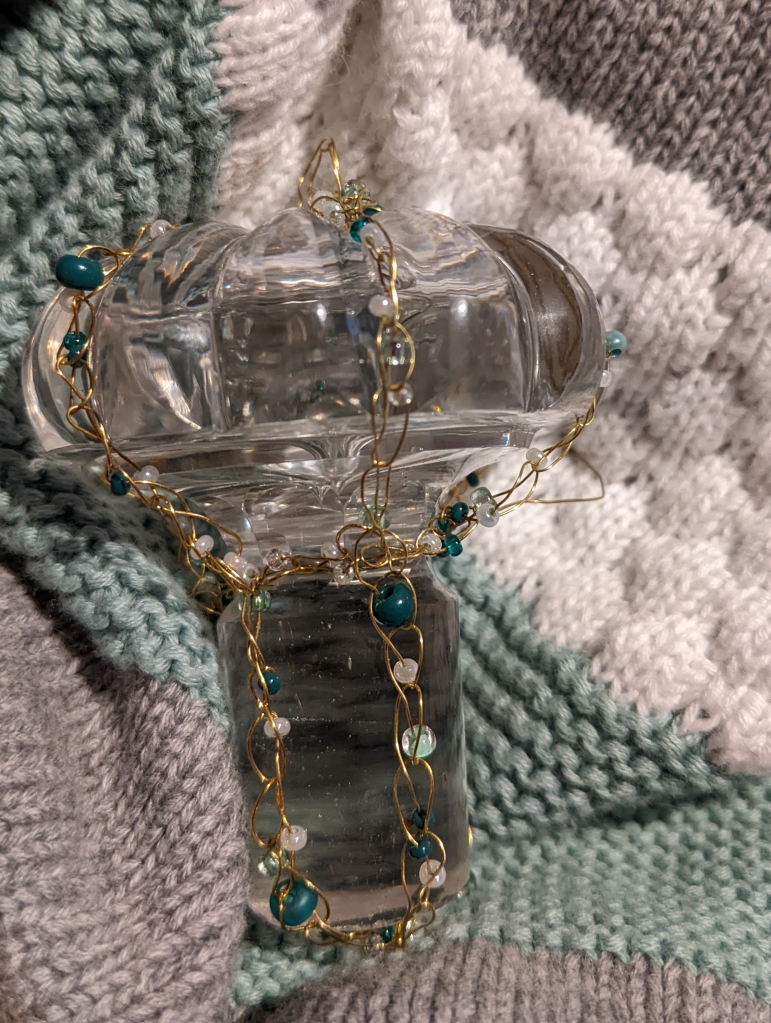 Mushroom shaped glass stopper caged in gold coloured wire with green and white beads 