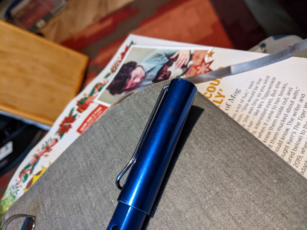 A blue fountain pen with the lid on, a closed notebook, and part of a magazine showing Judith Kerr with the original Mog 